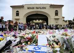 People stand near flowers laid as a tribute at Bondi Beach to honour the victims of a mass shooting that targeted a Hanukkah celebration at Bondi Beach on Sunday, in Sydney, Australia, December 16, 2025.