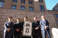 「無罪」と書かれた垂れ幕を掲げる日暮元社長(中央)ら=15日、横浜地裁