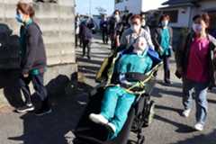 避難訓練でバギー型車いすに人形を載せて移動する参加者=小松島市田浦町