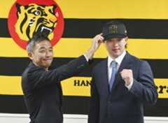 現役ドラフトでヤクルトから阪神に移籍し、帽子をかぶせてもらう浜田（右）＝12日、兵庫県西宮市