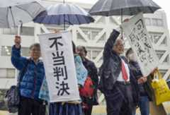 伊方原発3号機の運転差し止めが認められず、松山地裁前で「不当判決」などと書かれた垂れ幕を掲げる原告ら＝18日午後