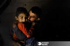 入植者の襲撃で住む場所を追われ、洞窟で生活するムハンマド・アブアラムさん（右）。暗闇の中、穏やかな表情で息子のイスマイル君を抱きしめた＝２０２５年８月２８日、ヨルダン川西岸マサフェルヤッタ（共同）