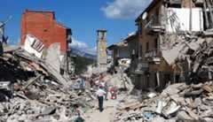Photograph of ruined buildings and piles of rubble with an intact clock tower still standing in the background. People walk among the rubble.