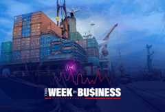A large cargo ship at a port, stacked with shipping containers and surrounded by cranes. The foreground features a graphic with the words "This Week in Business" styled with a city skyline and financial chart themes.
