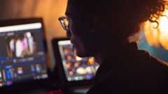 Person with long hair in bun and glasses in front of multiple monitors
