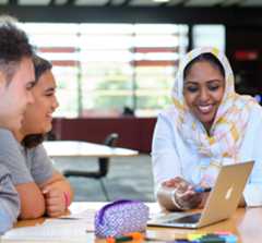 Students and librarian gathered around a table learning to use the library on a laptop screen