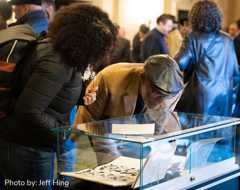 Decorative image showing two people standing over a glass exhibit box peering in to look closer at a book on display.