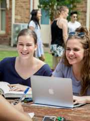 College students, happy and working with a book and laptop outdoors.