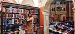 A woman is standing and reading a book while overlooking the main reading room