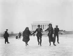 One man and two women are holding hands while ice-skating in front of the Lincoln Memorial.