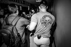 People take photos of a federal agent leading a man down a hallway.