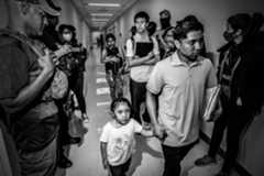 People walk down a hallway. They are surrounded by federal agents.