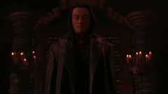 Darkly lit dungeon-y scene; hooded figure with visible face saying 'flawless victory'