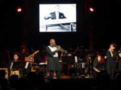 A trumpeter plays center stage surrounded by an ensemble.