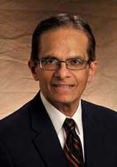 Headshot of Belle Upadhyaya wearing a black suit jacket, white dress shirt, and a black and red striped tie.