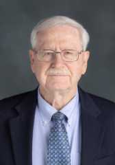 Headshot of Laurence Miller wearing a black suit jacket and light purple button-up dress shirt with a tie. 