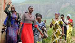 A half-dozen East African women smile and laugh as they walk by farm fields