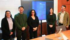 A team of students and a faculty director stand in a line before the projected cover of their report on the assassination of Berta Cáceres.