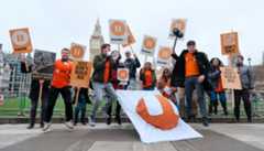 A couple dozen protesters jump in the air while holding signs that say 