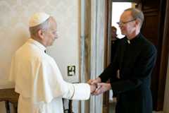 University President Rev. Robert A. Dowd, C.S.C., in black clerical attire, broadly smiles while shaking hands with Pope Leo XIV, a smiling man in white papal robes and a white zucchetto.