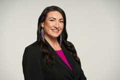 Angie Bruce wearing a black jacket and fuchsia top and wearing beaded earrings.