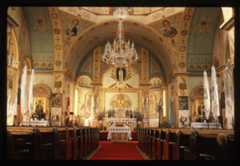 East wall and apse of Ukrainian Catholic Church with detailed wall art and red carpet between pews