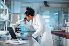 A researcher looks into a microscope in a biomedical lab.