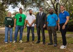 President Diaz stands beside five military affiliated students under some trees on campus.