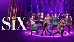 Six women performing on stage, dressed in vibrant costumes with purple lighting.