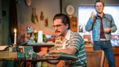 A man types at a desk, surrounded by kitchen items and a candle.