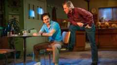 Two men interact at a table, one in a blue shirt, the other in a red shirt.