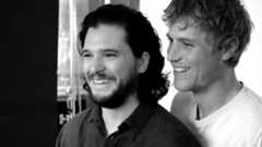 Two men smiling together in black and white, with a blurred background.