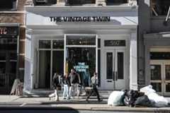 Articles of clothing hanging in a shop window with an inverted sign spelling out “THE VINTAGE TWIN.”