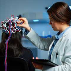 Woman patient wearing performant eeg headset scanning brain electrical activity in neurological research laboratory while medical researcher adjusting it, examining nervous system typing on tablet.