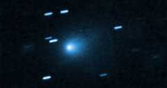 A bright blue comet with a glowing center is surrounded by streaks of light against a dark background, representing stars appearing as trails due to the motion of the comet.