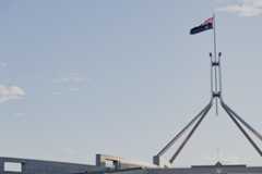 The flag on top of Parliament House, pictured from a distance, against a grey sky. The flag is on a big triangular flagpole.