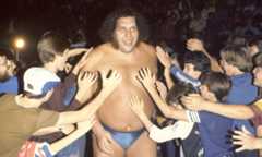Andre the Giant waling through a crowd of fans on the way to the ring. Fans are all reaching out to touch him.