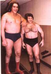 Andre the Giant with his arm on the shoulder of Bruno Sammartino in their wresting trunks next to a concrete wall