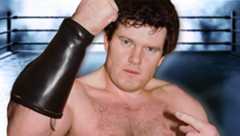 Professional wrestling Iron Mike Sharpe pointing at himself with his left hand while raising his right, clenched fist in the air.