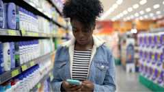 Young woman walking and using mobile phone in supermarket