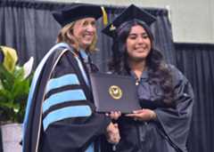 Two women shake hands and hold a diploma on stage.