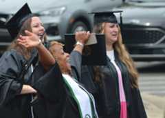 A female graduate throws her hands up in victory as two other female graduates smile