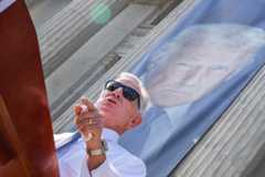Sen. Tommy Tuberville, R-Ala., speaks during a news conference outside USDA headquarters in Washington. A banner depicting President Donald Trump hangs behind him. 