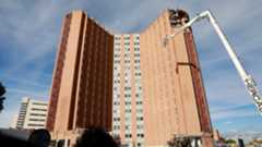 La capital de España asiste al derrumbe progresivo de uno de sus hitos más reconocibles. El Hospital público 12 de Octubre de la Comunidad de Madrid ha entrado en la fase decisiva de su Plan Integral de Modernización de Infraestructuras con la demolición de la antigua Residencia General, una emblemática torre de dieciocho plantas. Esta estructura, que ha sido parte del horizonte urbano de Madrid durante más de medio siglo, ya está empezando a convertirse en añicos.El proceso de remodelación, que se inició en 2021 durante la peor fase de la pandemia, afronta ahora su etapa más visible: la Fase 2 del Plan de Modernización, que comenzó a principios de este año tras concluir el traslado de la actividad asistencial al Nuevo Hospital en diciembre del año pasado.La demolición es descrita como una operación "casi quirúrgica". Para ello, se está utilizando la grúa de demolición más grande de España, equipada con una pluma de 62 metros capaz de alcanzar las plantas más altas. Previamente, durante los meses anteriores, se derruyeron las construcciones bajas cercanas a la torre y se vació el edificio principal para facilitar su destrucción. El objetivo de los técnicos es que para finales del mes de enero la célebre torre del 12 de octubre sea solo un recuerdo.Aunque la torre desaparece, la directora gerente de la institución, la doctora Carmen Martínez de Pancorbo, reconoce que hay "Tenemos sentimientos encontrados". Destaca que la torre fue un icono, "una silueta muy reconocible y parte del horizonte urbano de nuestro Madrid", y que fue la cuna de "hitos muy importantes de la sanidad pública madrileña y española".A pesar de la magnitud de la obra, la Comunidad asevera que el reto de no repercutir en la actividad sanitaria se está cumpliendo, pues la atención asistencial del 12 de Octubre se está prestando "con normalidad".El espacio liberado por la mítica torre dará paso a una "nueva etapa" con infraestructuras que estarán "mucho más apropiadas" para los retos de las próximas décadas. El nuevo proyecto contempla que el espacio libre se transforme en amplias zonas verdes. Estas áreas no solo tendrán un valor estético, sino también un «objetivo terapéutico», y buscan conectar mejor el hospital con su entorno. Con estas acciones "Se romperán barreras visuales", fusionando el campus del 12 de Octubre con las áreas de recreo próximas, culminando la reurbanización de la parcela para facilitar el tránsito de peatones y vehículos.