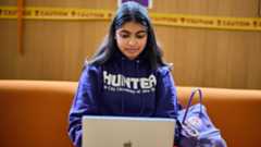 Hunter student wearing CUNY sweatshirt working on laptop in Student Union