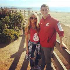Two WSU Cougs dressed in WSU Coug gear in front of a guardrail at the beach.