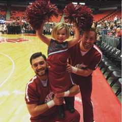 A child dressed as a WSU cheerleader with two WSU cheerleaders on the basketball court.