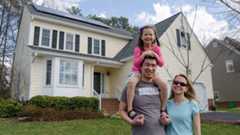 A family smiling in front of their solar home.