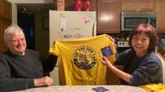 Larry and Angie Johnson smiling and holding a SUN shirt and sticker.