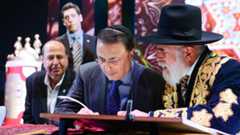 Bukharian billionaire Lev Leviev, center, writing in a Torah scroll with Rabbi Eliyahu Yaakov, right, and Israel's then-defense minister Moshe Yaalon, in Jerusalem, March 23, 2014. (Israel Barddougo/World Congress of Bukhara Jews/JTA)